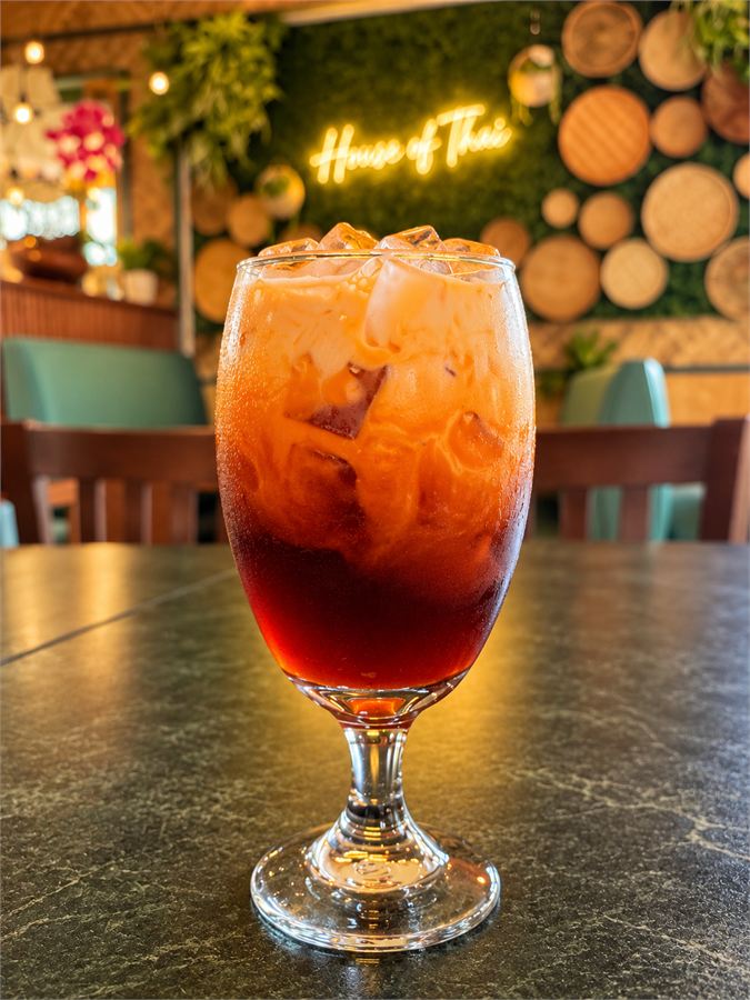 Thai iced tea in front of the House of Thai neon sign